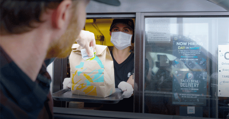 A Taco Bell drive-thru customer receives his order on a tray from an employee in a mask and gloves