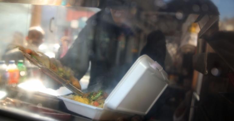 A New York City food cart worker fills a plastic foam container with food for a customer