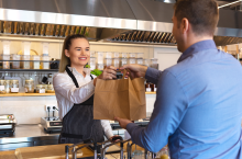 Happy-waitress-waring-apron-serving-customer-at-counter-in-small-family-eatery-restaurant.-Small-business-and-entrepreneur-concept-with-woman-owner-in-eatery-with-takeaway-service-delivery-1127824238_5800x3866.png